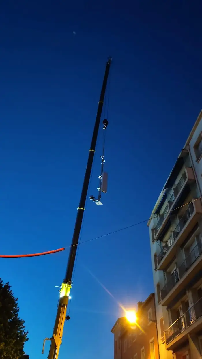 Levage d’équipement télécom par grue à Lyon de nuit Grue soulevant un équipement télécom en pleine nuit à Lyon